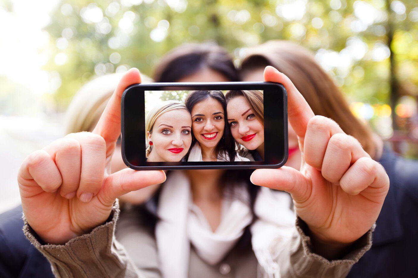 Three students holding up phone to take selfie outside