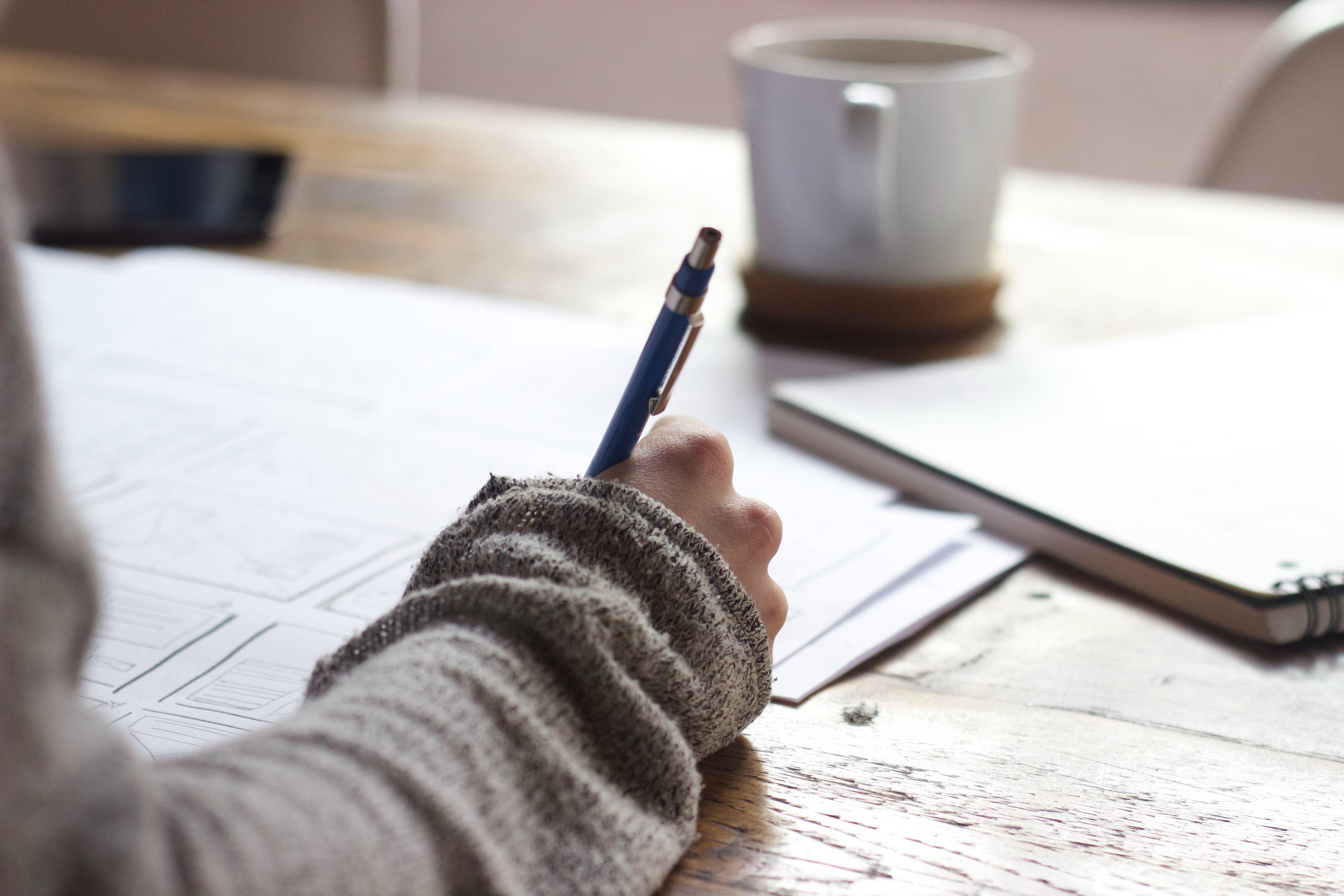 person wearing a sweater, writing with a pencil