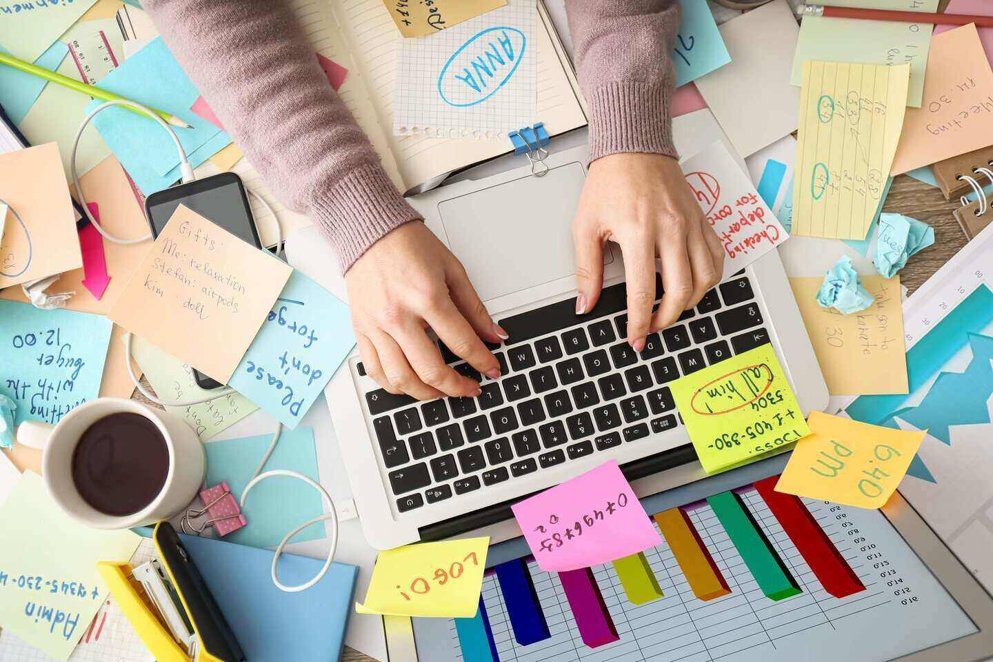 Hands on laptop keyboard with colorful post-its, graph chart, coffee cup