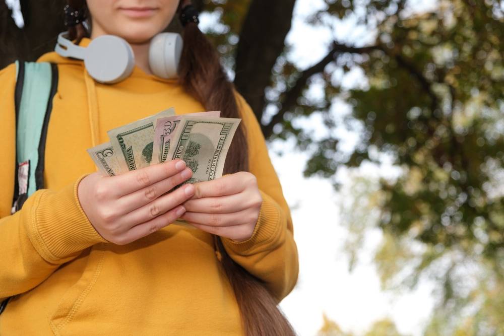 A teenage girl with headphones counts dollar bills