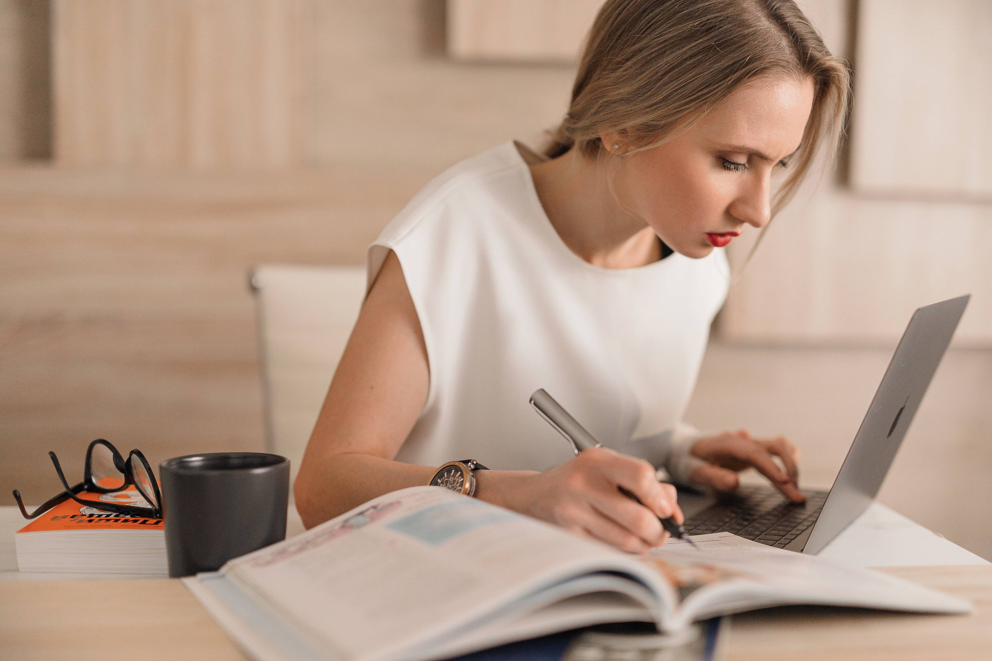 woman concentrating on a laptop with an open book