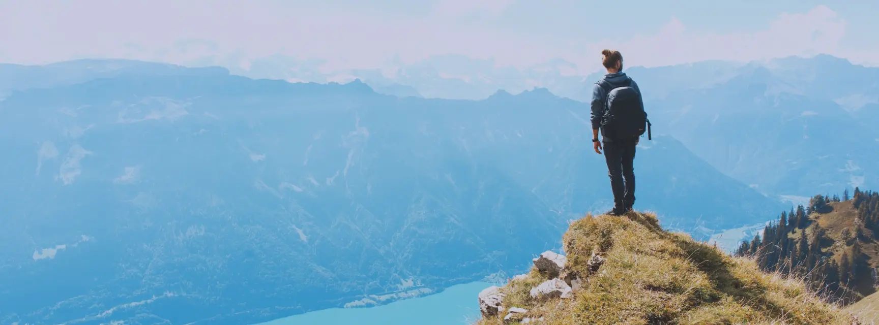 Mountaineer standing on top of a peak overlooking the lake and mountains