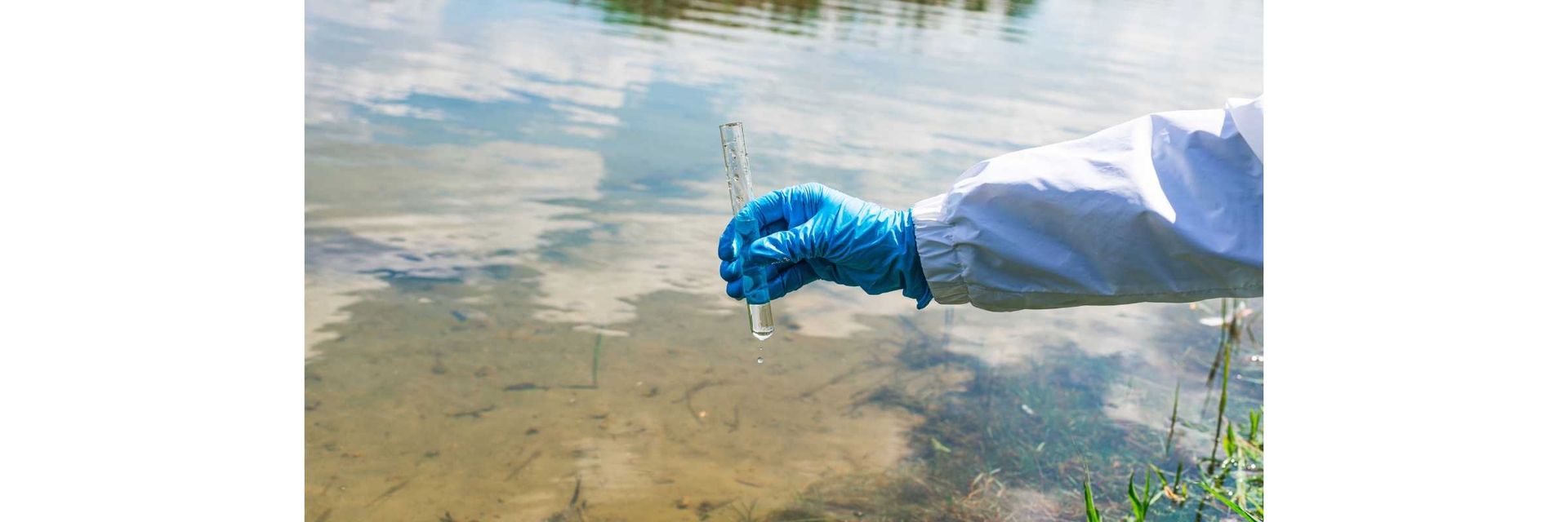 arm with a medical glove and white lab coat holding a test tube over a stream