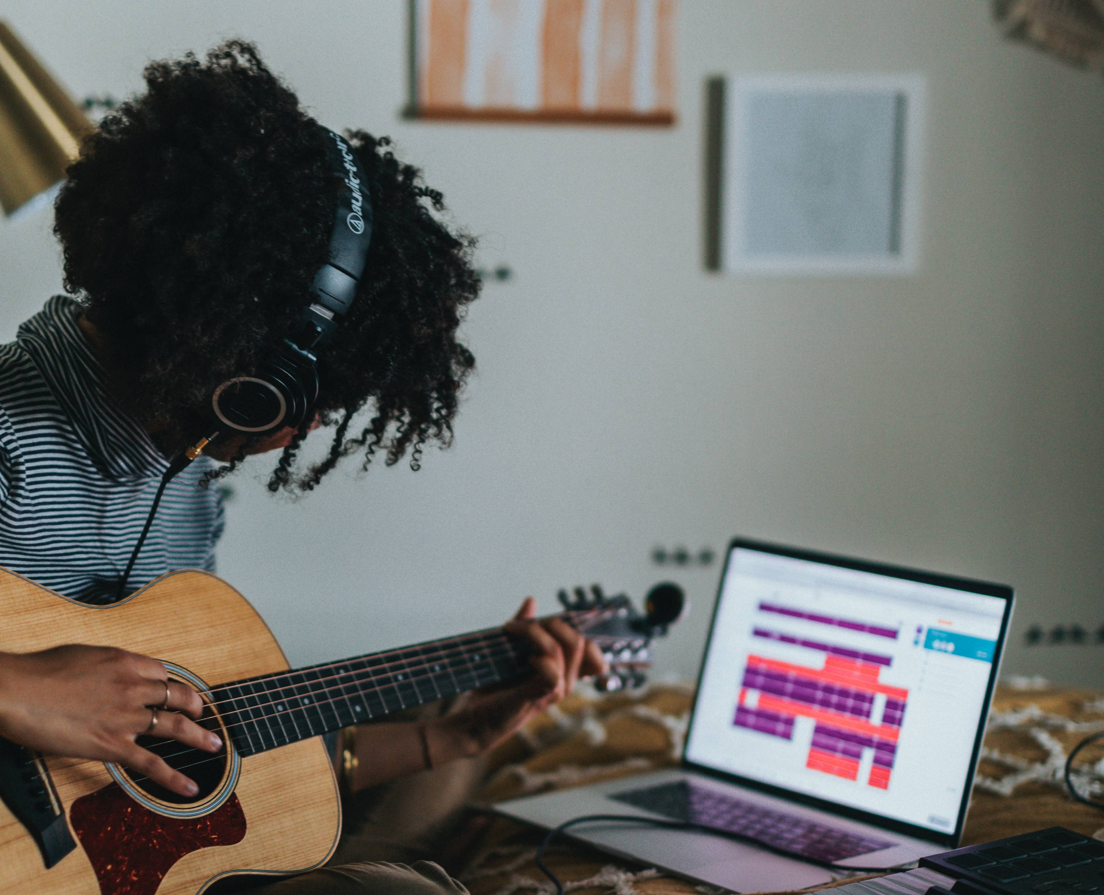 student playing guitar and looking at a computer