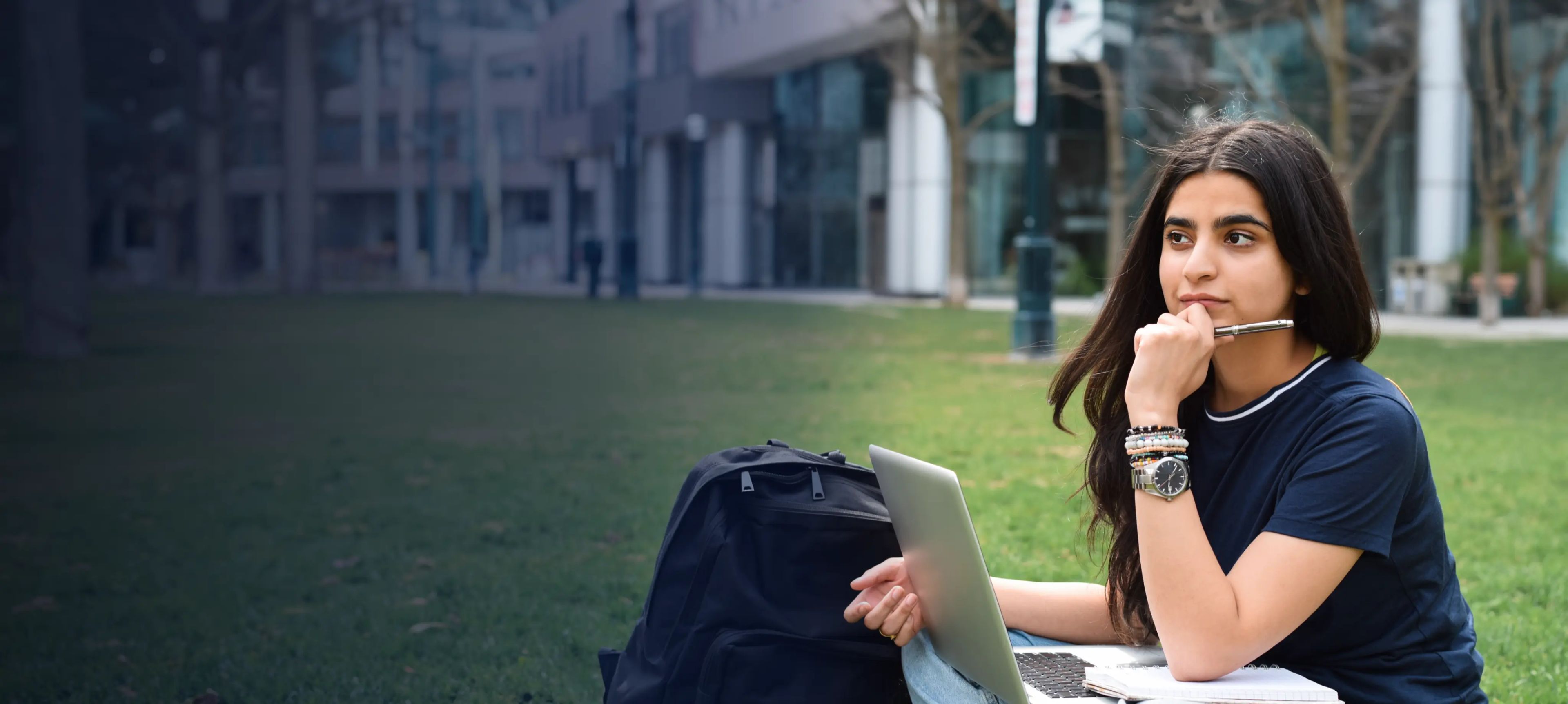 Young female student sitting on green lawn using laptop computer