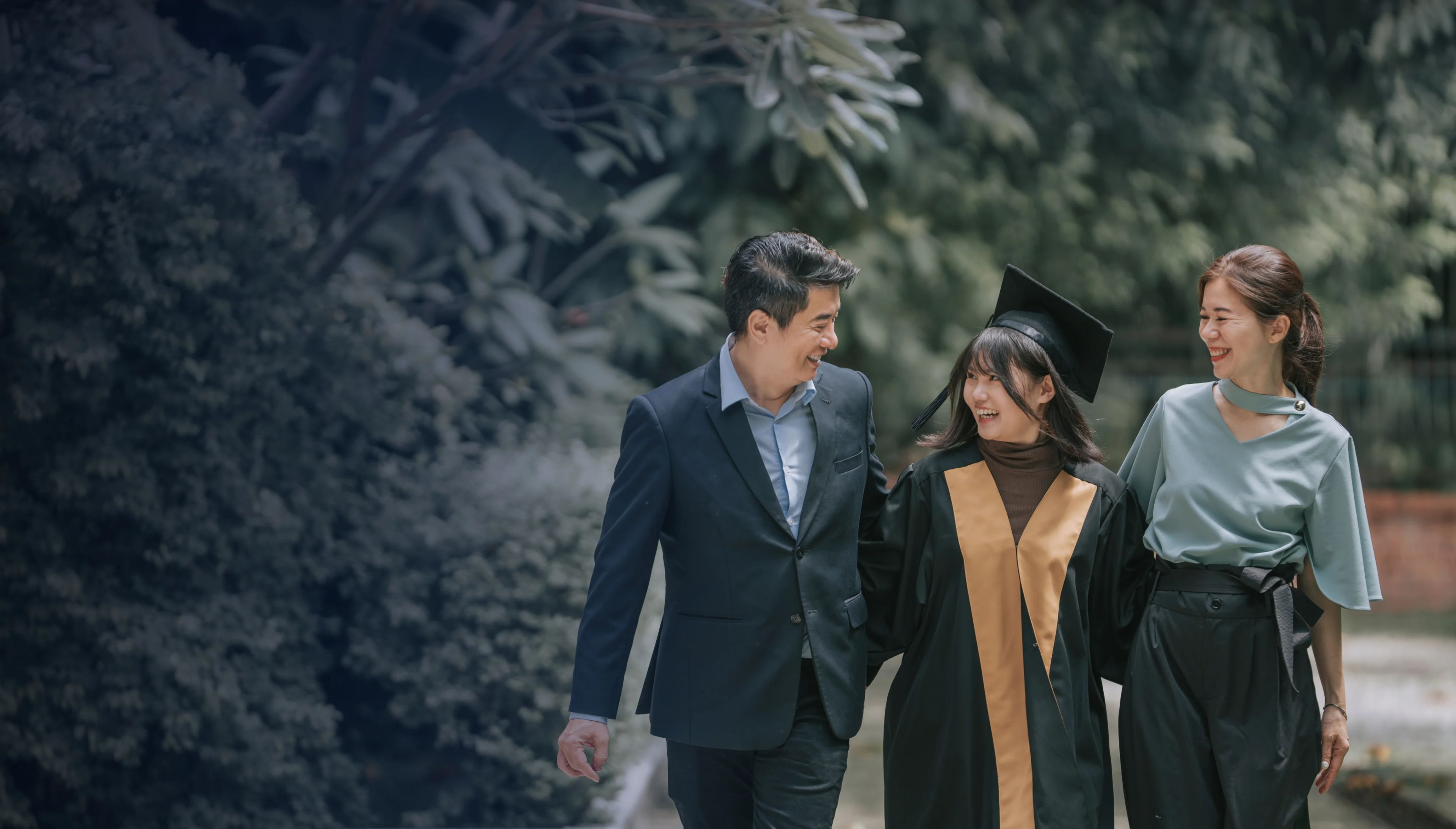 Proud parents walking together with daughter with graduation gowns