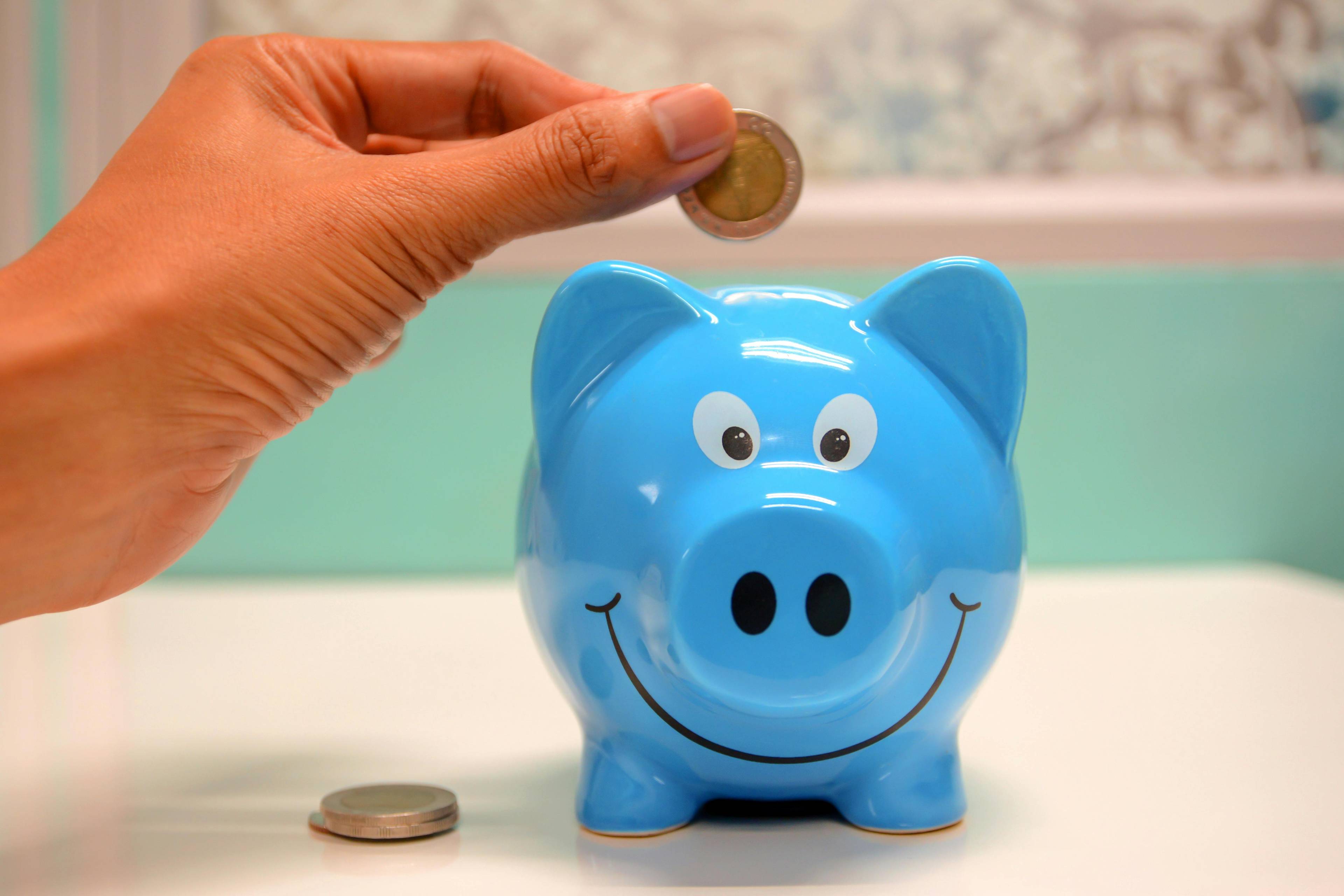 a hand placing a coin in a blue piggy bank