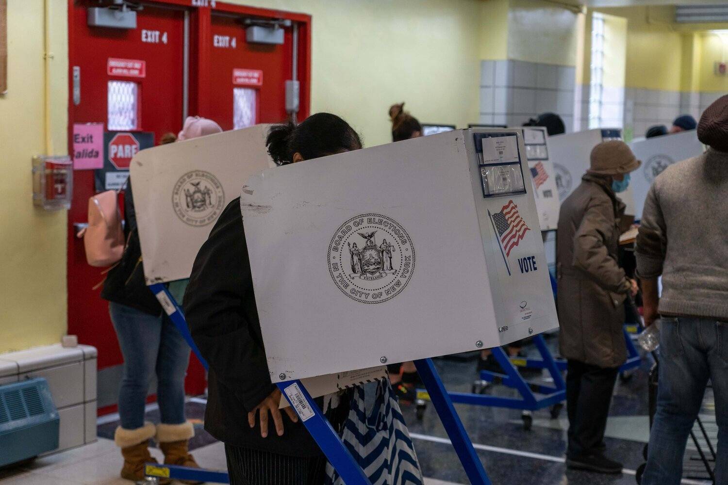 Many people behind privacy voting machines; one wearing mask