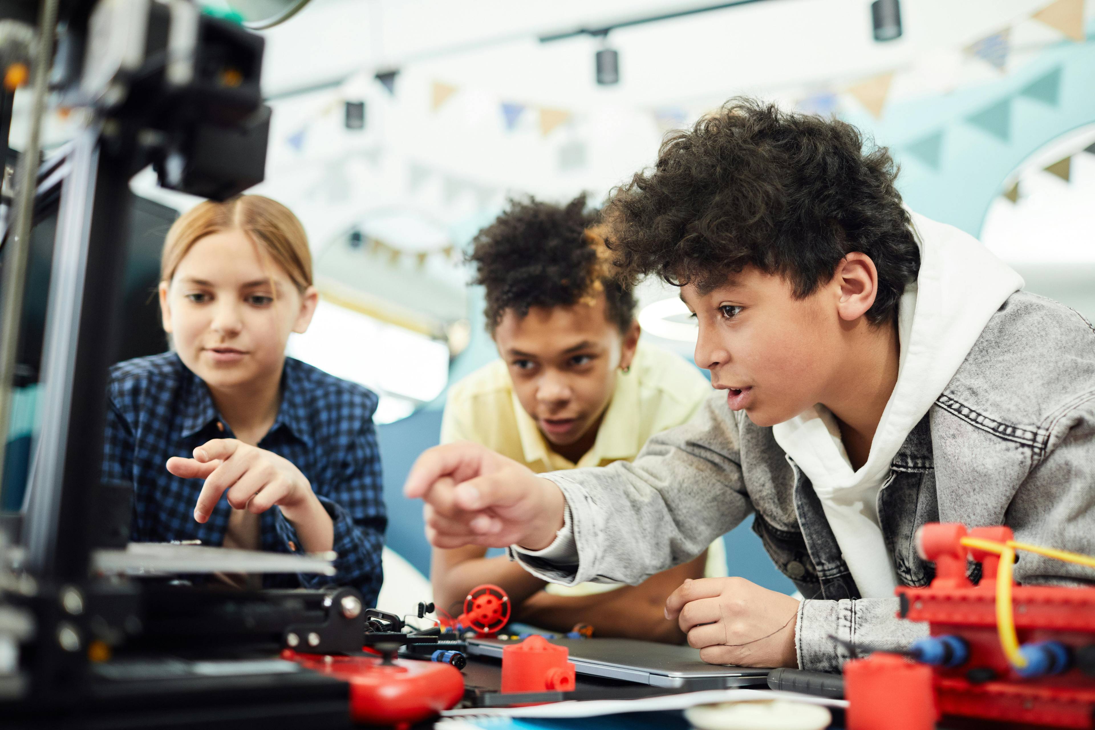 Three students using a 3D printer in a school setting. 