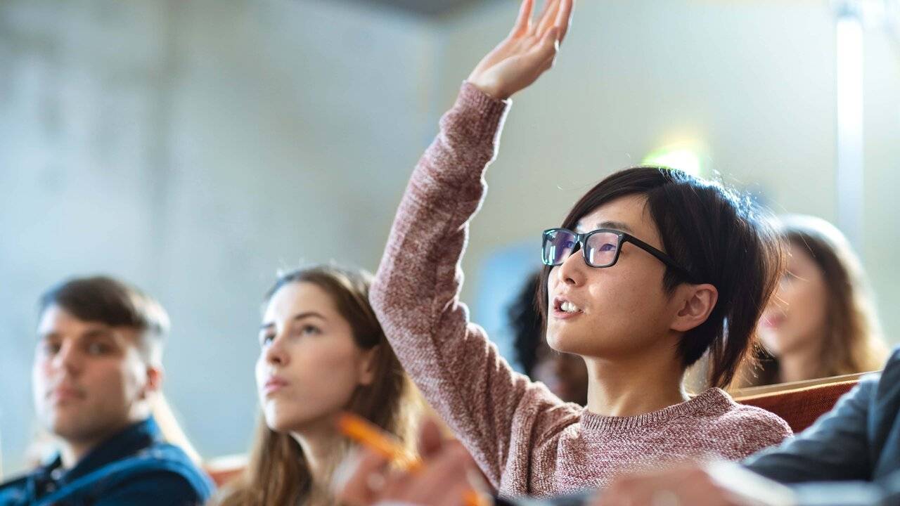 Image of multiple students  sitting in classroom style with one raising hand